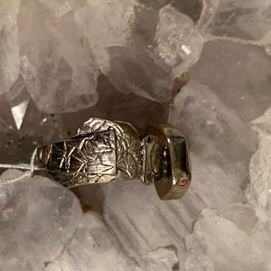 May include: A silver ring with a textured band and a square-shaped gemstone.