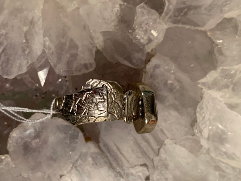 May include: A silver ring with a textured band and a square-shaped gemstone.