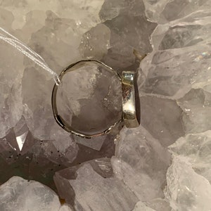 May include: A silver ring with a dark gray oval gemstone. The ring is sitting on a bed of white crystals.