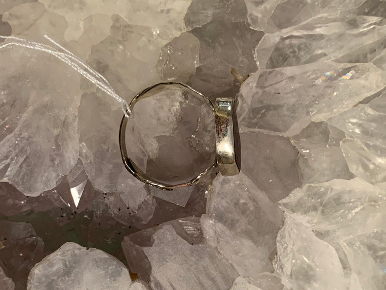 May include: A silver ring with a dark gray oval gemstone. The ring is sitting on a bed of white crystals.