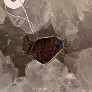 May include: A silver ring with a dark blue opal stone set in a silver band. The ring is surrounded by white crystals.