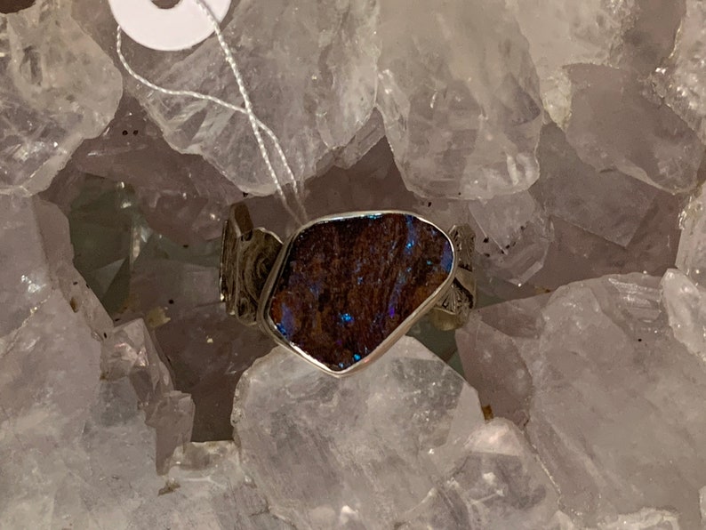 May include: A silver ring with a dark blue opal stone set in a silver band. The ring is surrounded by white crystals.