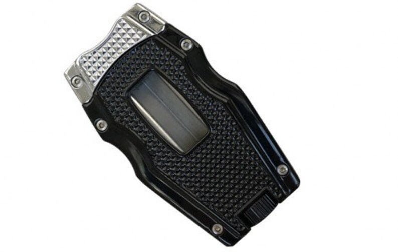 May include: A black and silver cigar cutter with a textured grip and a silver blade. The cutter has a diamond pattern on the top and a black and silver design on the bottom.