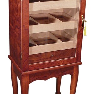 May include: A mahogany wood humidor with a glass door and a hygrometer on the top. It has four shelves and a drawer. The humidor is on four legs with a decorative design.