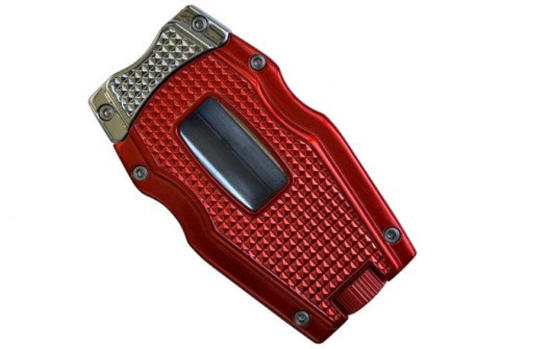 May include: Red metal cigar cutter with a silver top and a diamond pattern. The cutter has a built-in lighter.