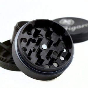 May include: A black metal grinder with a circular grinding chamber and a small metal disc in the centre. The grinder has a textured outer ring and a smooth inner ring.