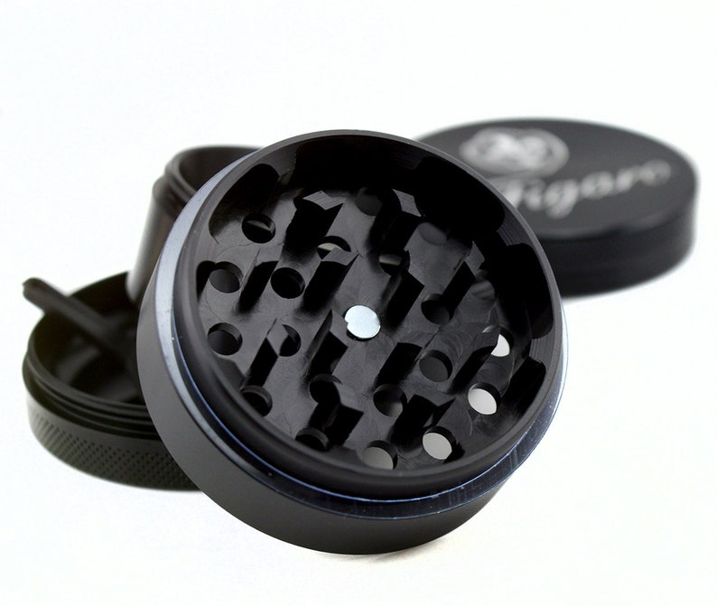 May include: A black metal grinder with a circular grinding chamber and a small metal disc in the centre. The grinder has a textured outer ring and a smooth inner ring.