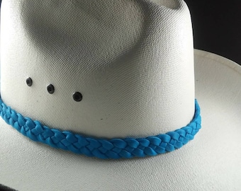 May include: A white cowboy hat with a turquoise braided band. The hat has a classic brim and a structured crown with three small black rivets. The hat is set against a dark background.