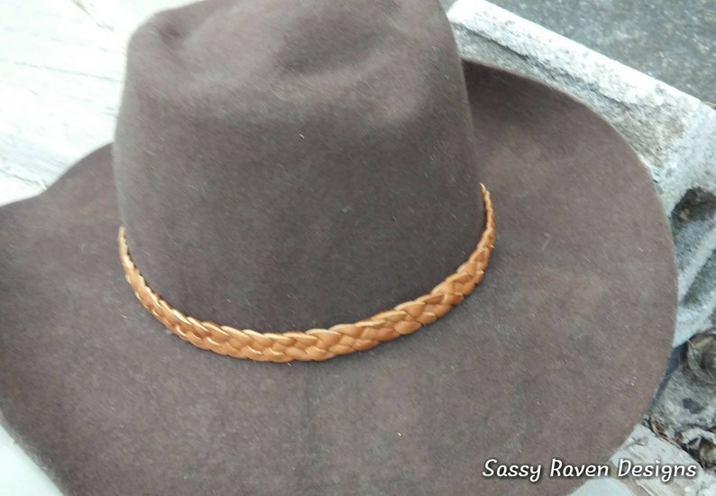May include: A brown felt hat with a braided leather band. The hat has a wide brim and a classic cowboy hat style. The hat is a neutral color and would be suitable for many outfits.