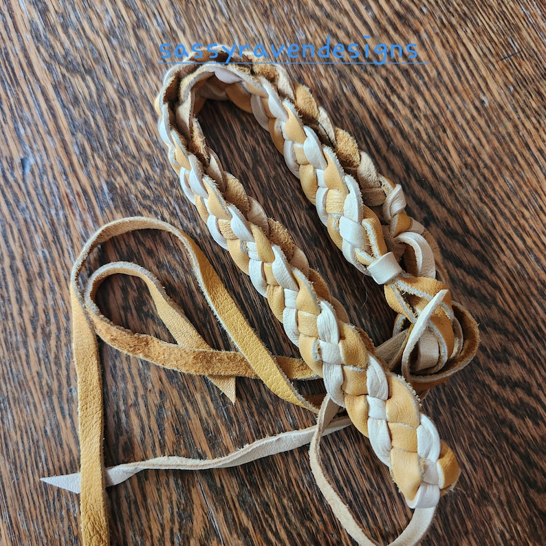 May include: Braided leather strap in shades of tan and cream, with a long, thin leather tie. The strap is made of interwoven strips of leather, creating a textured pattern. The text "ssyLaVerdeDesigns" is visible in the image.