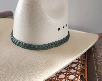 May include: A white cowboy hat with a dark green braided band and black stitching around the crown.