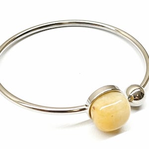 May include: A silver bangle bracelet with a yellow stone and a silver bead.
