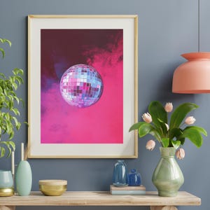May include: A framed print of a silver disco ball against a pink and purple background.