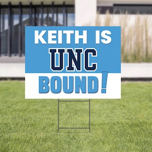 Może przedstawiać: Prostokątny znak z napisem "KEITH IS UNC BOUND!" w kolorze białym i niebieskim. Znak znajduje się na metalowej ramie i jest umieszczony na zielonym trawniku. Tło obejmuje dom i rozmyty krajobraz.