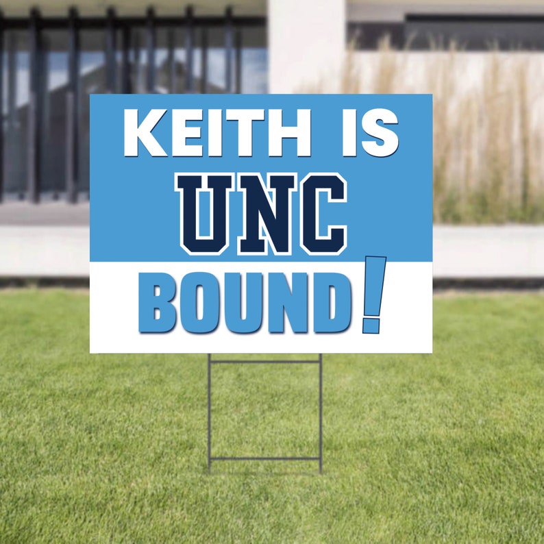 Może przedstawiać: Prostokątny znak z napisem "KEITH IS UNC BOUND!" w kolorze białym i niebieskim. Znak znajduje się na metalowej ramie i jest umieszczony na zielonym trawniku. Tło obejmuje dom i rozmyty krajobraz.