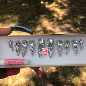 May include: A set of ten silver press-on nails with a pointed shape and a design of iridescent rhinestones. A small tube of nail glue is included.