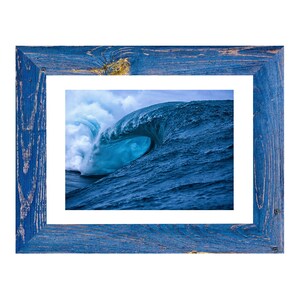 May include: A framed photograph of a large ocean wave, captured in shades of blue and white. The wave is breaking, creating a tunnel-like shape. The frame is made of distressed blue wood, adding a rustic touch to the artwork.