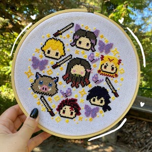 Könnte beinhalten: Ein Kreuzstich-Stickrahmen mit Anime-Charakteren. Das Design zeigt Figuren mit Schwertern, lila Schmetterlingen und gelben Sternen. Der Rahmen wird von einer Hand gehalten.