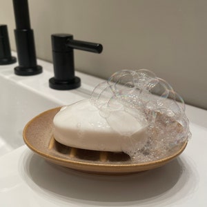 May include: A white bar of soap with bubbles on top, sitting in a brown ceramic soap dish.