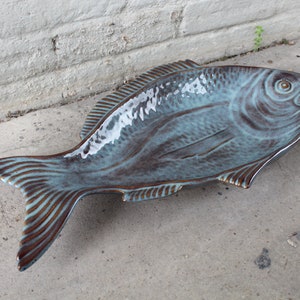 May include: A ceramic fish-shaped serving dish with a teal glaze and brown accents. The dish is glazed in a mottled pattern, giving it a rustic look.