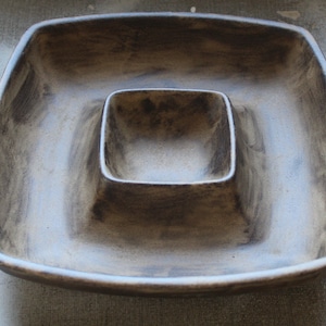 May include: A brown ceramic serving dish with a square shape and a smaller square-shaped dip in the center.