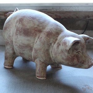 May include: A ceramic pig figurine with a white and brown mottled glaze. The pig is standing on all four legs with its head turned to the side.