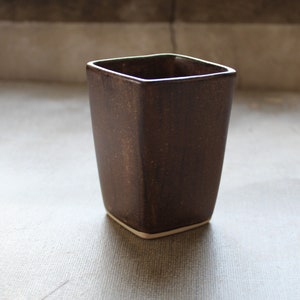 May include: A square brown ceramic cup with a white rim. The cup is speckled with brown and white flecks.