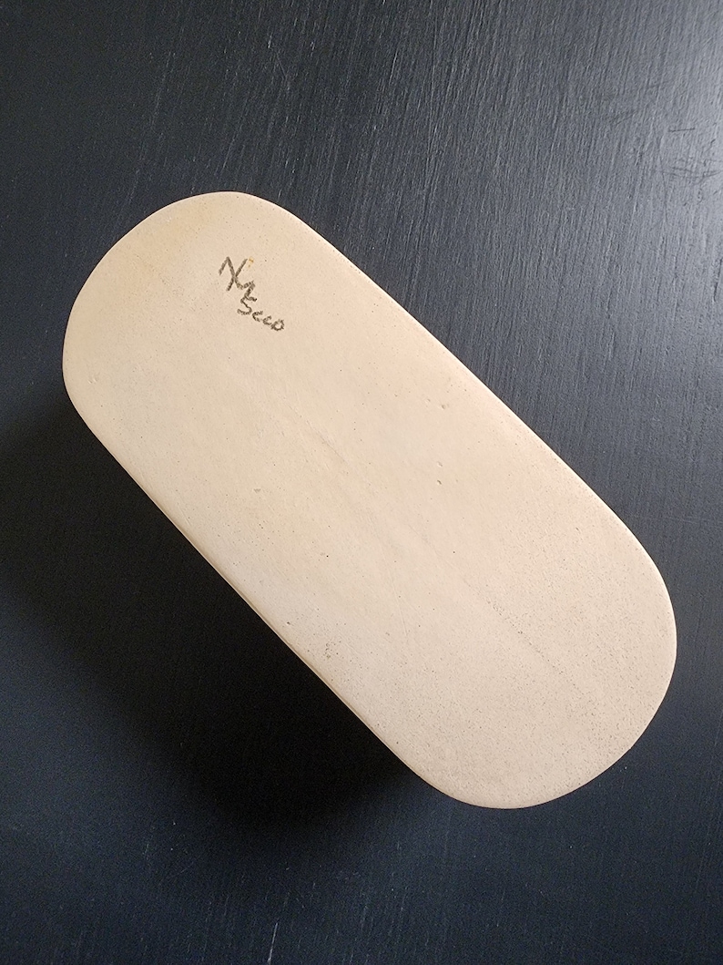 May include: A light beige oval-shaped wooden board with a handwritten signature that says "M. Secco".