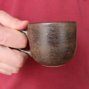 May include: A brown ceramic mug with a speckled glaze. The mug has a rounded shape and a handle.