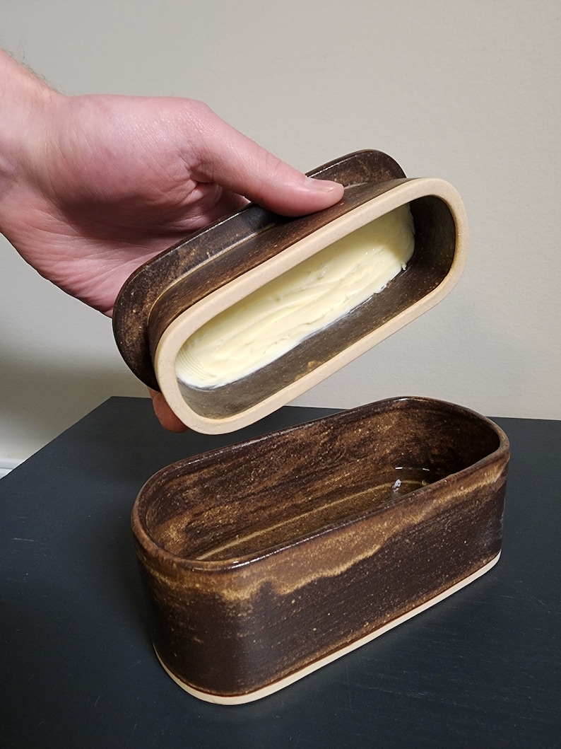 May include: A brown ceramic butter dish with a lid. The lid is open and the dish is filled with butter.
