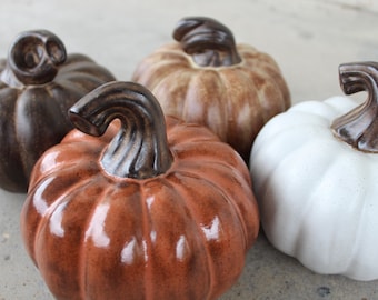May include: Four ceramic pumpkins in different colors: brown, orange, tan, and white. The pumpkins are all hand-painted and have a glossy finish.