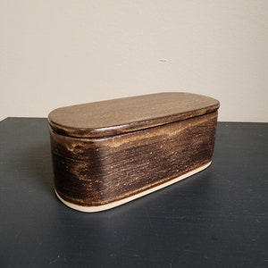 May include: A brown ceramic butter dish with a lid. The dish has a slightly oval shape and a white rim.