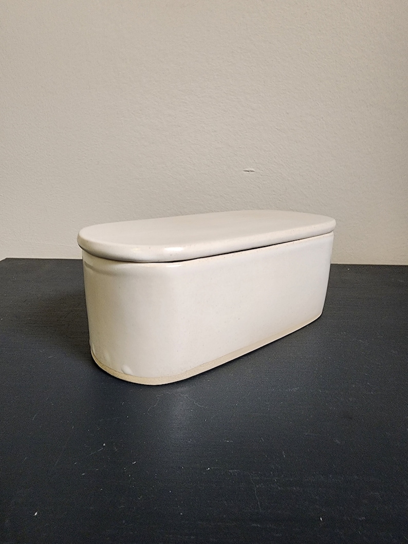 May include: A white ceramic butter dish with a lid. The dish is oval shaped and has a smooth, glossy finish.