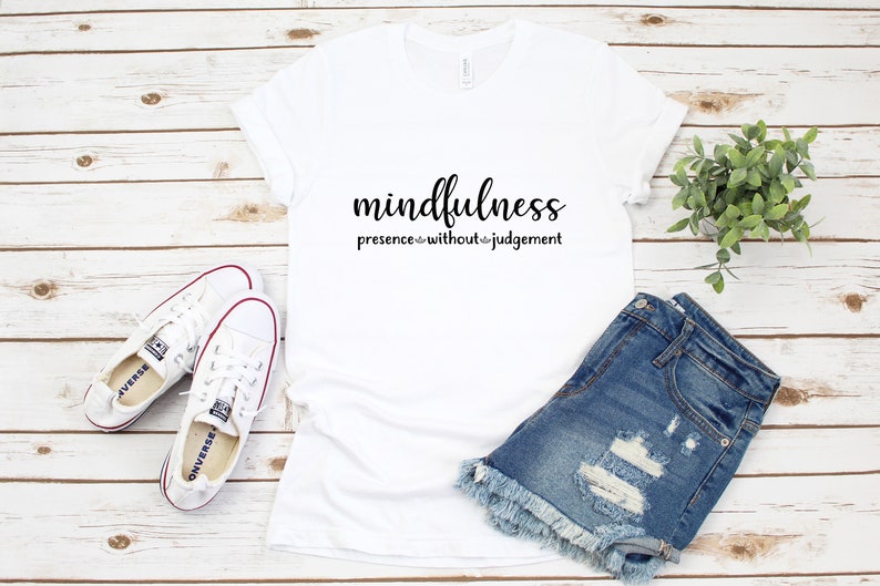 以下が含まれることがあります： 黒で「mindfulness presence without judgement」とプリントされた白いTシャツ