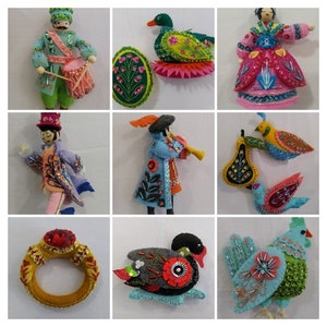 May include: A collection of handmade felt ornaments, including a drummer, a figure in a coat, a musician playing a wind instrument, a ring, a duck, a rooster, and birds. The ornaments feature intricate beadwork and colorful designs.
