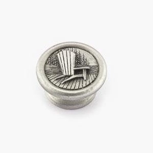 May include: A silver-toned metal knob with a raised design of a chair on a porch. The knob is round and has a smooth surface.