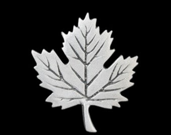 May include: A silver-colored metal maple leaf ornament. The leaf is detailed with veins and a textured surface.