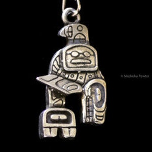 May include: Silver pendant featuring a stylized Native American design with a bird and a human figure. The pendant is detailed with geometric patterns and has a loop for attaching a chain.