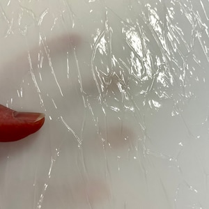 May include: A close-up of a clear, textured plastic sheet with a slight sheen. The sheet is wrinkled and has a crinkled appearance.