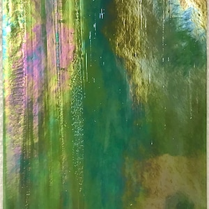 May include: A close-up of a green, iridescent glass tile with a textured surface. The tile has a subtle shimmer and a variety of shades of green, including teal, olive, and emerald.