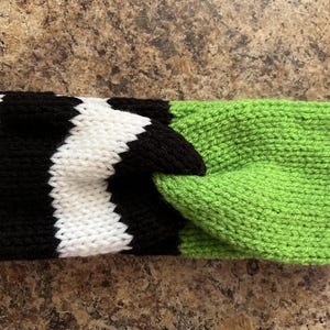 May include: A knitted headband with a twisted design. The headband features a black and white striped pattern on one side and a solid bright green color on the other. The item is made of a soft, textured yarn.