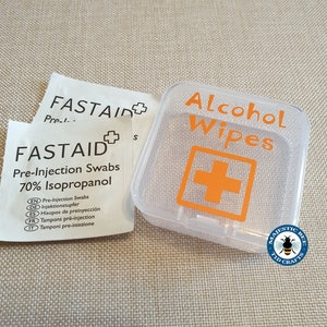 K&ouml;nnte beinhalten: Ein durchsichtiger Plastikbeh&auml;lter mit einem wei&szlig;en Etikett, auf dem "Alcohol Wipes" und ein orangefarbenes Pluszeichen stehen. Der Beh&auml;lter ist mit dem Firmennamen "Majestic Bee T1D Crafts" gekennzeichnet.