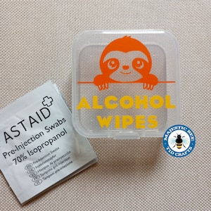 May include: A clear plastic container with a sloth design and the text "ALCOHOL WIPES". The container is labelled with the text "MAJESTIC BEE TID CRAFTS". A small white packet of pre-injection swabs is also shown in the image.