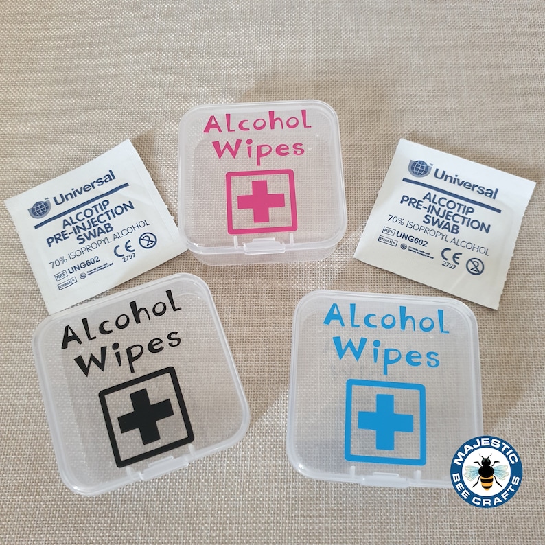 K&ouml;nnte beinhalten: Vier durchsichtige Plastikbeh&auml;lter mit dem Text "Alcohol Wipes" und einem Pluszeichen in verschiedenen Farben. Die Beh&auml;lter sind mit dem Text "Alcohol Wipes" und einem Pluszeichen in Schwarz, Pink, Blau und Schwarz beschriftet. Die Beh&auml;lter befinden sich auf einer braunen Oberfl&auml;che.