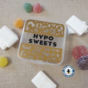 May include: A clear plastic container with a gold and black leopard print design. The container has the text "HYPO SWEETS" printed on it. The container is surrounded by colourful sweets.