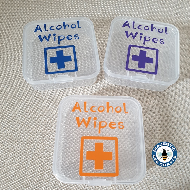 K&ouml;nnte beinhalten: Drei transparente Plastikbeh&auml;lter mit dem Text "Alcohol Wipes" und einem roten Kreuz darauf gedruckt. Die Beh&auml;lter sind mit einem blauen, violetten und orangefarbenen Kreuz gekennzeichnet.