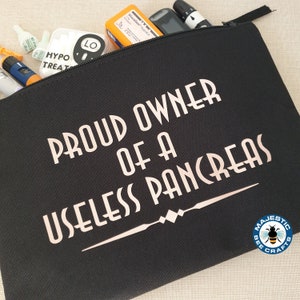 May include: Black canvas zippered pouch with the text "Proud Owner of a Useless Pancreas" in white lettering. A small bee logo with the text "Majestic Bee Crafts" is in the bottom right corner.