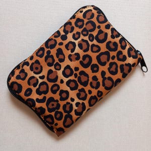 May include: A brown and black leopard print zipped pouch. The pouch is made of a soft, fabric material.