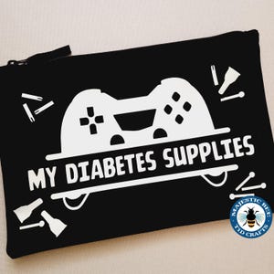 May include: Black zippered pouch with the text "MY DIABETES SUPPLIES" and a white graphic of a video game controller. The pouch also features white graphics of medical supplies. The Majestic Bee Tid Crafts logo is in the bottom right corner.