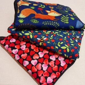 May include: Three zipped pouches stacked. The top pouch is navy blue with an orange fox and green foliage. The middle pouch is navy blue with red strawberries and yellow bees. The bottom pouch is black with red and pink hearts.